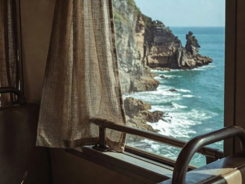 Woven window curtain and metal handrail inside a Vietnamese train overlooking coastal cliffs
