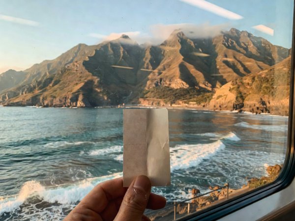 Taiwan Railways ticket stub held against a carriage window overlooking coastal mountains